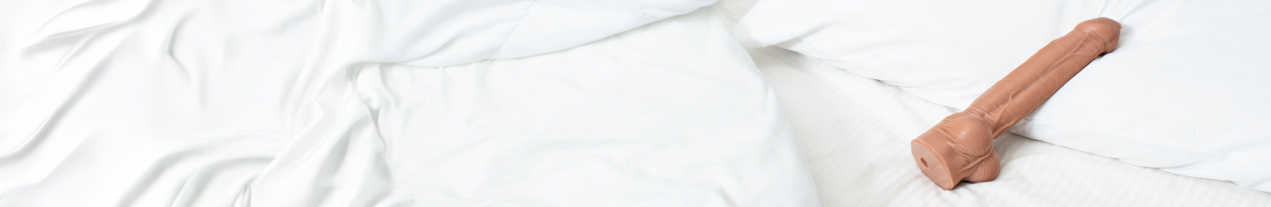 A handcrafted silicone dildo lying on white bedding, showcasing ultra-realistic detailing.